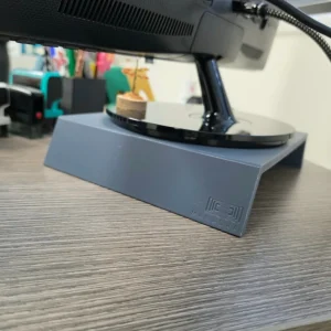 Support d'écran de bureau Manaora en gris ardoise, logo Manaora gravé, placé sous un écran — imprimé en 3D à Tahiti
